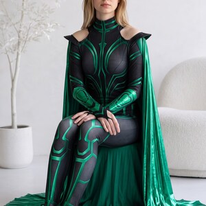 May include: A full-body costume featuring a black and metallic green bodysuit with a textured, honeycomb-like pattern and geometric green accents. The outfit includes a high-neck design, cold-shoulder cutouts, and a long, flowing metallic green cape.