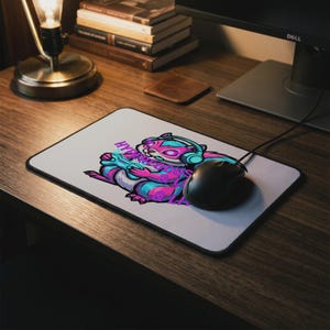 May include: A rectangular mouse pad featuring a graphic of a squirrel wearing headphones and holding a game controller. The design uses vibrant pink and blue colors with the text HYPERFOCUS & LIL printed in a stylized font across the center.