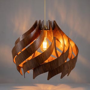 Puede incluir: Una lámpara colgante que presenta una serie de listones de madera de color marrón oscuro curvados, dispuestos en una forma esférica en espiral. Una bombilla estilo Edison cuelga en el centro, suspendida por una varilla metálica recta de color latón.