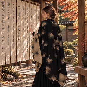 Puede incluir: Un chal reversible en negro y beige con un patrón repetitivo de hojas de ginkgo en tono dorado. La prenda tiene un cuello alto y cae sobre los hombros, mostrando un exterior oscuro con motivos de hojas claros y un interior en contraste.