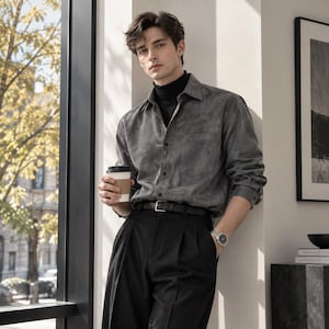 Pode incluir: Uma camisa de manga comprida cinza-carvão abotoada sobre uma gola alta preta, combinada com calças pretas plissadas e um cinto de couro preto. Um relógio de pulso prateado com mostrador escuro no pulso esquerdo e um copo de café de papel.