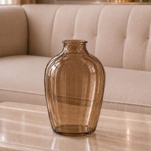May include: A translucent, amber-colored glass vase with a rounded body and a narrow neck. The vase features a subtle vertical ribbed texture throughout its surface, creating a series of light-catching lines that run from the base to the rim.