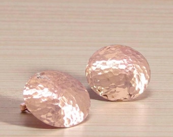 Könnte beinhalten: Ein Paar runde Ohrstecker aus Roségold mit einer gehämmerten, strukturierten Oberfläche, die das Licht reflektiert. Die Ohrringe haben eine konvexe, kuppelartige Form und eine polierte metallische Oberfläche mit einem markanten Dellenmuster.