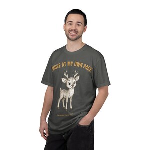 Puede incluir: Una camiseta gris oscuro con una ilustración de dibujos animados de un cervatillo con manchas blancas y astas. Sobre el cervatillo, el texto dice "I MOVE AT MY OWN PACE." y debajo, "Generator Energy Type." en una fuente de color dorado.
