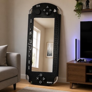 Puede incluir: Un espejo de pie alto y rectangular diseñado para parecerse a una consola de juegos portátil Sony PSP negra. El marco presenta botones de juego icónicos, una cruceta y el texto "PSP" y "SONY" impresos en blanco sobre la superficie.