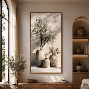 Può includere: Una stampa artistica da parete rettangolare verticale che presenta una natura morta composta da tre vasi in ceramica beige di diverse altezze. Un sottile ramo di ulivo con foglie verdi emerge dal vaso più alto, proiettando ombre morbide.