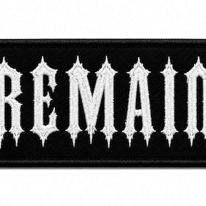 Puede incluir: Un parche rectangular bordado con fondo negro y borde blanco. La palabra REMAIN está cosida en el centro con una tipografía gótica blanca y dentada, con bordes afilados y puntiagudos en las letras, creando un diseño de alto contraste.
