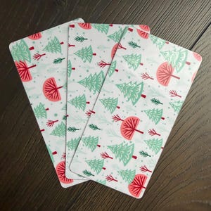 May include: Three rectangular bookmarks featuring a white background with a repeating pattern of light green evergreen trees, dark green pine sprigs, and rounded coral pink trees. The bookmarks have rounded corners and a smooth, flat surface finish.