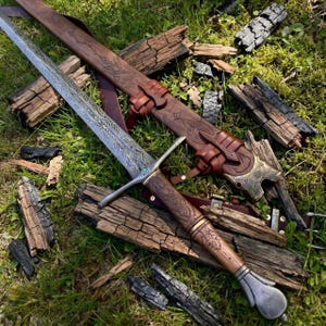 May include: A double-edged sword with a patterned steel blade, a crossguard featuring a small green stone, and a brown leather-wrapped handle. The sword is accompanied by a matching brown leather scabbard with intricate embossed designs.