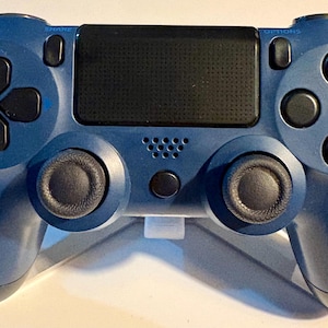 May include: A blue video game controller featuring a central black touchpad, two black analog sticks, a directional pad, four action buttons, and buttons labeled SHARE and OPTIONS. The device has a speaker grill and a small circular button below it.