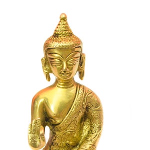 Peut inclure: Une statue en laiton dorée représentant un Bouddha assis. Le Bouddha porte une robe et a une expression sereine sur son visage. La statue est finement détaillée et possède une base avec un motif décoratif.