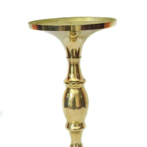May include: A gold metal candle holder with a wide base and a tall, slender stem. The holder has a smooth, polished finish.