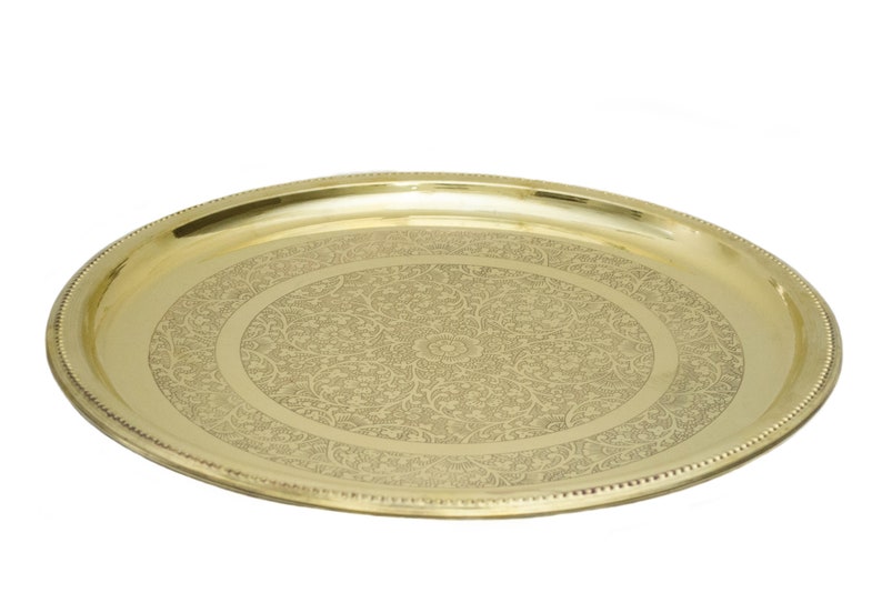 May include: A gold-colored, oval serving tray with an intricate floral pattern etched into the center. The tray has a beaded edge and a polished finish, suitable for decorative or functional use.
