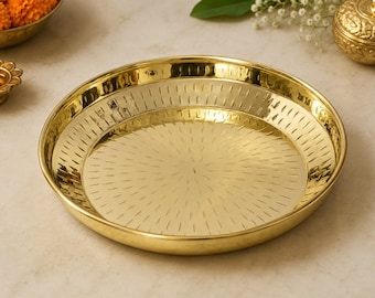 May include: A round, polished brass plate featuring a shallow basin and a slightly raised rim. The interior surface of the plate is decorated with a repeating pattern of small, etched vertical dashes that radiate outward from the center.