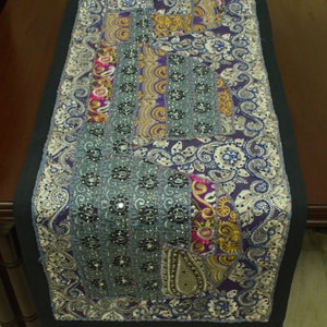 May include: A purple and blue table runner with intricate embroidery and sequins. The runner features a patchwork design with various floral and paisley patterns.