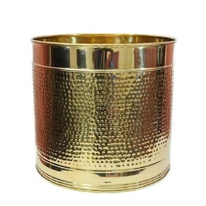 Peut inclure: Un cache-pot cylindrique en laiton avec une finition polie et une surface martelée texturée. Le récipient présente un bord supérieur plat et lisse ainsi qu'une base assortie, affichant une teinte dorée métallique réfléchissante sur l'extérieur.