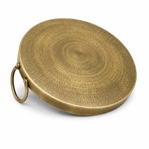 May include: A circular brass tray with a textured, hammered surface featuring concentric rings of small indentations. The tray has a smooth, raised edge and a single, round brass handle attached to one side, allowing for easy lifting and carrying.