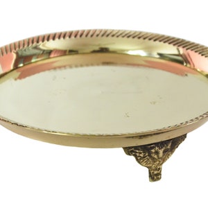 Op de afbeelding: Een gouden metalen dienblad met een decoratieve rand en drie sierlijke poten.