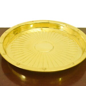 Puede incluir: Una bandeja redonda de servir de metal dorado con un patr&oacute;n decorativo de rayos de sol. La bandeja tiene una superficie lisa y brillante.