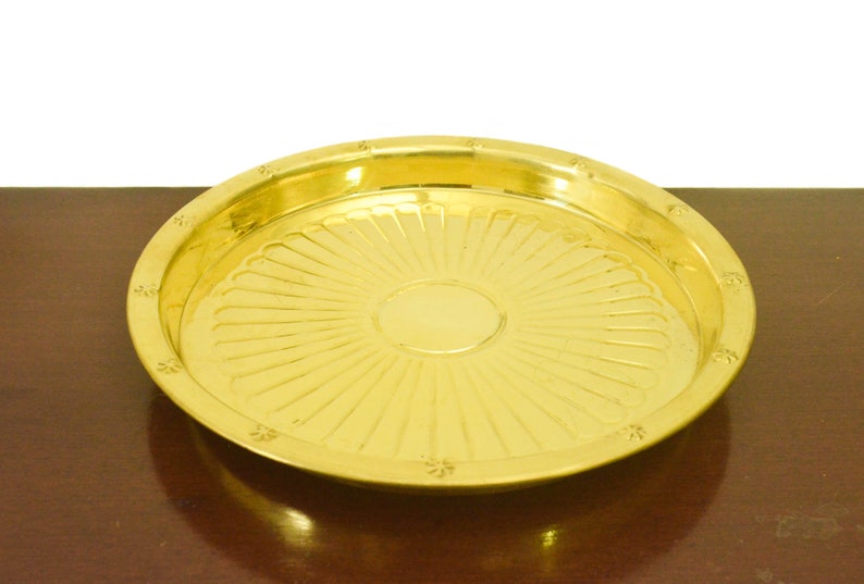Puede incluir: Una bandeja redonda de servir de metal dorado con un patr&oacute;n decorativo de rayos de sol. La bandeja tiene una superficie lisa y brillante.