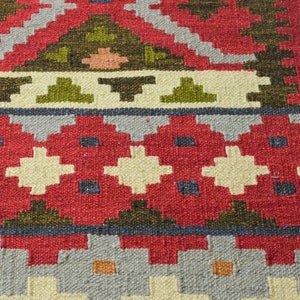 May include: Close-up of a red, white and green patterned rug with a geometric design. The rug is woven with a variety of textures and colours.