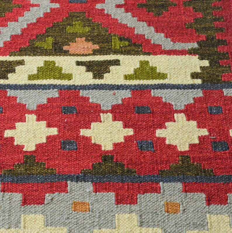 May include: Close-up of a red, white and green patterned rug with a geometric design. The rug is woven with a variety of textures and colours.