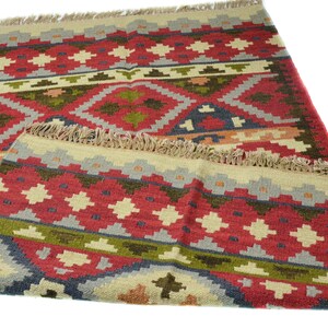May include: A red, green and beige patterned rug with a fringe border. The rug has a geometric design with diamond shapes.