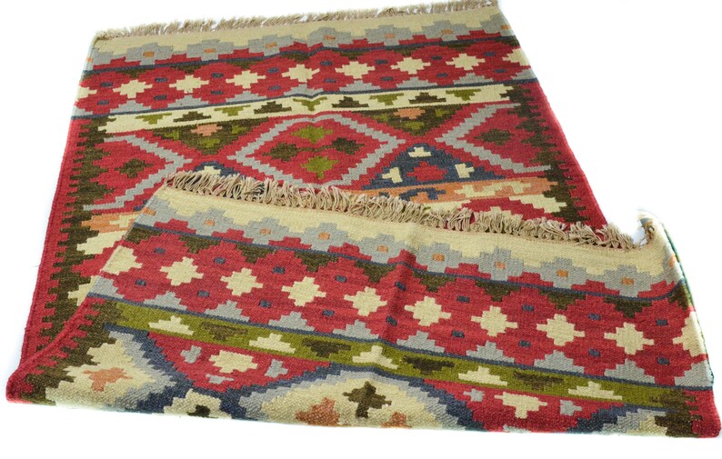 May include: A red, green and beige patterned rug with a fringe border. The rug has a geometric design with diamond shapes.