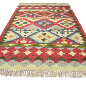 May include: A colourful, geometric patterned rug with a red, green, blue, and beige colour scheme. The rug has a fringe border.