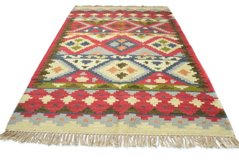 May include: A colourful, geometric patterned rug with a red, green, blue, and beige colour scheme. The rug has a fringe border.