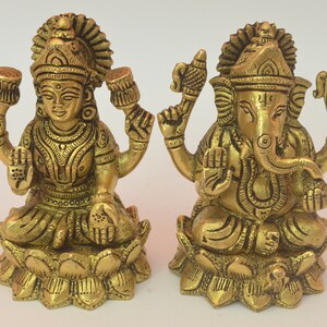 Peut inclure: Deux statues en m&eacute;tal dor&eacute; repr&eacute;sentant les divinit&eacute;s hindoues Lakshmi et Ganesha, assises sur des bases en forme de lotus. Les statues sont finement d&eacute;taill&eacute;es et pr&eacute;sentent un style indien traditionnel.