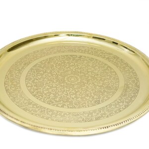 May include: A gold-colored, oval serving tray with an intricate floral pattern etched into the surface. The tray has a beaded edge and a polished finish, suitable for decorative or functional use.