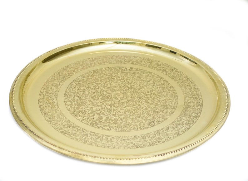 May include: A gold-colored, oval serving tray with an intricate floral pattern etched into the surface. The tray has a beaded edge and a polished finish, suitable for decorative or functional use.
