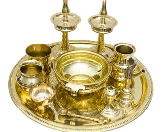 May include: A set of brass puja items on a round tray. The set includes a bowl, two oil lamps, a small pot, a spoon, a small incense burner, and two small cups.