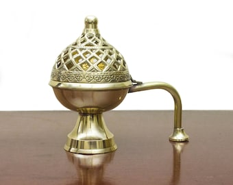 May include: A gold metal incense burner with a decorative, openwork design. The burner has a handle and sits on a round base.