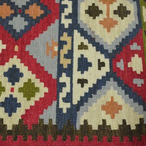 May include: A close-up of a colourful rug with a geometric pattern. The rug is made of wool and has a variety of colours, including red, blue, green, and beige.