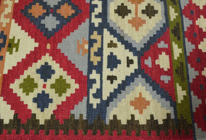 May include: A close-up of a colourful rug with a geometric pattern. The rug is made of wool and has a variety of colours, including red, blue, green, and beige.