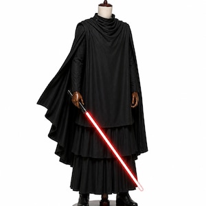 May include: A black long-sleeved tunic with a high neckline, a layered skirt, and a flowing cape draped over the shoulders. The outfit is paired with a black handle prop featuring a glowing red light blade extending downwards from the right hand.
