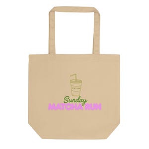 May include: A beige tote bag featuring a centered graphic of a green line-art matcha drink in a cup with a straw. Below the cup, the text reads Sunday in green cursive script and MATCHA RUN in large, bold, pink capital letters.
