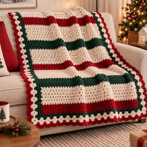 Puede incluir: Una manta rectangular de ganchillo con rayas horizontales en colores alternos crema, verde bosque y rojo intenso. La manta está rematada con un borde decorativo festoneado en crema y rojo, creando un diseño de borde con textura.