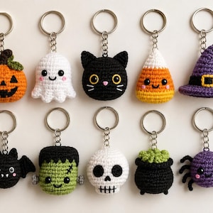 Könnte beinhalten: Eine Sammlung von zehn gehäkelten Schlüsselanhängern mit Halloween-Motiven, darunter ein Kürbis, ein Geist, eine schwarze Katze, ein Zuckermais, ein Hexenhut, eine Fledermaus, ein Monster, ein Totenkopf, ein Kessel und eine violette Spinne.