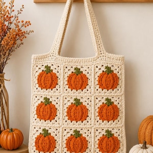 May include: A cream-coloured crochet tote bag featuring a grid of nine square panels. Each square contains a textured orange pumpkin with a green stem, crafted in a granny square style with two long shoulder straps for carrying items.