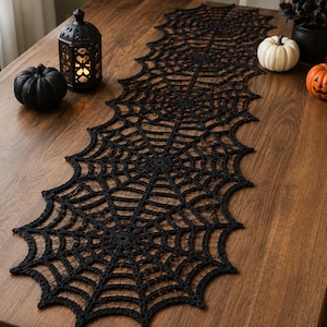 May include: A black lace table runner featuring a repeating spider web pattern with scalloped edges. The runner is elongated and crafted with intricate, open-work thread detailing that forms a series of connected circular web designs.