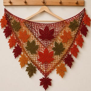 May include: A triangular crochet shawl featuring an openwork mesh pattern adorned with numerous three-dimensional maple leaf motifs in shades of deep red, burnt orange, and olive green, arranged in a symmetrical, cascading autumn-inspired design.