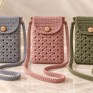 Puede incluir: Tres bolsos bandolera de ganchillo en azul claro, rosa empolvado y verde oliva. Cada bolso presenta un patrón de puntos texturizados en forma de estrella, una solapa plegable asegurada con un botón de madera clara y una correa a juego.