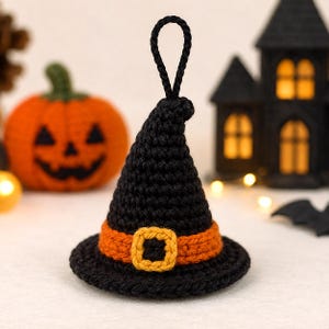 Peut inclure: Un ornement en forme de chapeau de sorcière crocheté en noir avec une bande orange et une boucle carrée jaune. Le chapeau présente un sommet pointu avec une boucle en fil noir pour le suspendre, révélant une texture en laine sur l'ensemble.