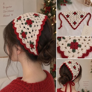Op de afbeelding: Een driehoekige gehaakte hoofddoek met een crèmekleurige basis en een herhalend patroon van rode en donkergroene bloemmotieven. De randen zijn afgewerkt met een geschulpte rode boord en lange linten aan de hoeken om het vast te maken.
