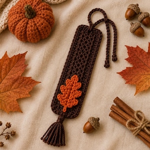 May include: A dark brown rectangular crochet bookmark featuring a small orange crocheted oak leaf appliqué and a matching dark brown tassel at the bottom. The bookmark includes a long dark brown crocheted cord loop at the top for securing pages.