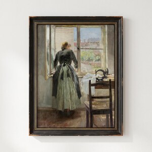 May include: A framed oil painting depicting a person standing at an open window, wearing a dark jacket and a long, light-colored skirt. A sewing machine sits on a wooden table next to a dark wooden chair, with a view of city rooftops visible outside.