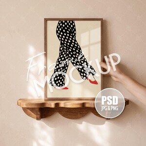 May include: A framed vertical print featuring a graphic illustration of legs wearing black trousers with white polka dots and red high-heeled shoes. The artwork is set against a cream-colored background and is displayed in a simple wooden frame.